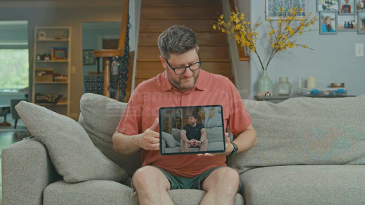 Man on Couch Watching Video on His Tablet of Another Man Sitting on His Couch