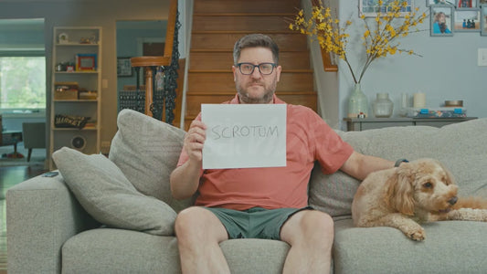 Man on Couch Holding a Piece of Paper That Says 'Scrotum' On It
