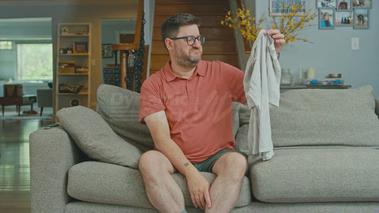 Man on Couch Holding Up a Plain White T-Shirt Dismissively