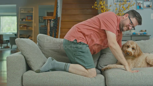 Man on Couch Tries to Do Yoga But Doesn't Know How Yoga Works Much to the Irritation of His Dog