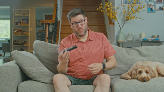 Man on Couch Removes Batteries from a Television Remote in a Playful Way While His Dog Looks On
