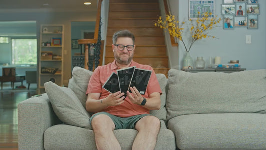 Man on Couch Admiring Framed Photos of His Three Children While His Dog Looks On