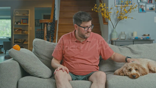 Man on Couch Pretends an Orange is a Telephone
