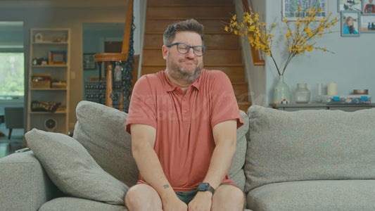 Man on Couch Giggling and His Dog Walks By